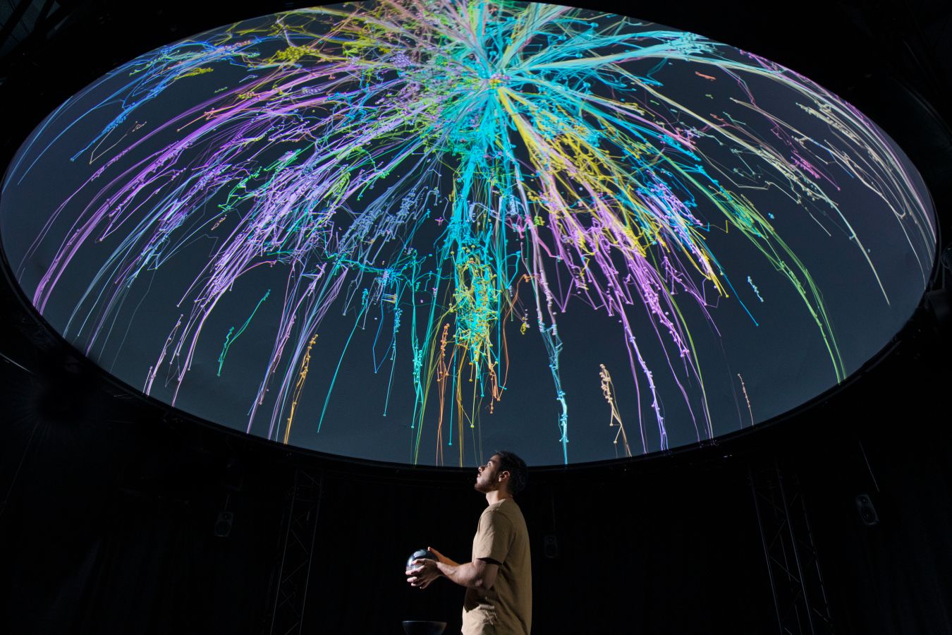 Man holding a remote control module in the shape of a ball, which controls an overhead display showing all the jazz music concerts recorderd at Montreux Jazz Festival, and which are organized by mood.